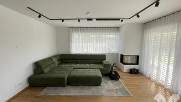 Gemütliches Wohnzimmer mit großem Ecksofa, Holzboden, Kamin und viel Tageslicht.