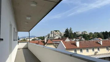 Langer Balkon mit Stadtblick und umliegenden Dächern unter bewölktem Himmel.