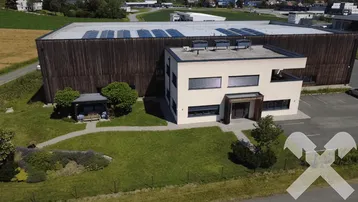 Luftaufnahme eines modernen Bürogebäudes mit angrenzender Lagerhalle, umgeben von Grünflächen und einem kleinen Pavillon.