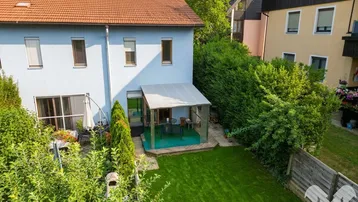 Hausrückseite mit gepflegtem Rasen, überdachter Terrasse und angrenzendem Gartenbereich.