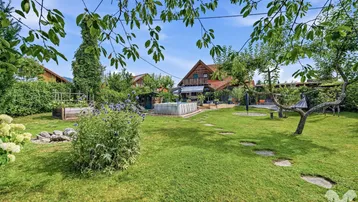 Weitläufiger grüner Garten mit Rasenfläche, Bäumen und einem kleinen Pool im Hintergrund.