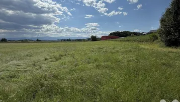 Weitläufiges grünes Feld unter blauem Himmel mit Blick auf entfernte Berge und ein Gebäude mit Solaranlage.