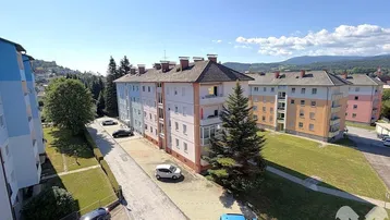 Weitläufige Ansicht von Wohngebäuden in einer grünen Umgebung mit Bergen im Hintergrund.