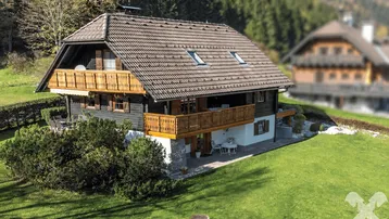 Traditionelles Chalet mit Holzbalkonen, Satteldach und großem Garten in ländlicher Umgebung mit Bergblick.
