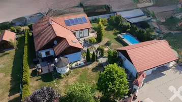 Luftaufnahme eines Anwesens mit mehreren Gebäuden, großem Garten und Swimmingpool unter blauem Himmel.
