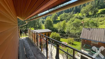 Blick vom Balkon auf die umliegende grüne Landschaft und die bewaldeten Hügel.