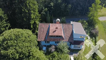 Luftaufnahme eines Hauses mit rotem Ziegeldach, umgeben von dichtem Grün und Bäumen.