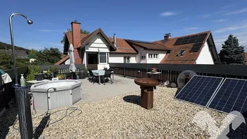 Große Dachterrasse mit Whirlpool, Sitzbereich und Solarpaneelen unter blauem Himmel.