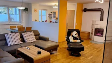 Geräumiger Wohn-Essbereich mit gemütlichem Sofa, Esstisch und einem traditionellen Kachelofen.