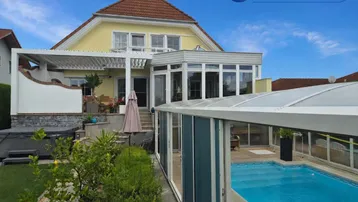 Großzügiger Außenbereich mit Hausfassade, überdachtem Pool und gepflegtem Garten.