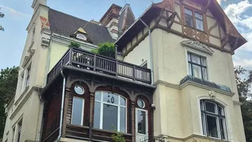 Historische Villa mit mehreren Balkonen und traditioneller Architektur unter bewölktem Himmel.