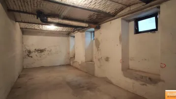 Unfertiger Kellerraum mit Betonboden, freiliegenden Rohren und kleinen Fenstern, ideal als Lagerfläche.