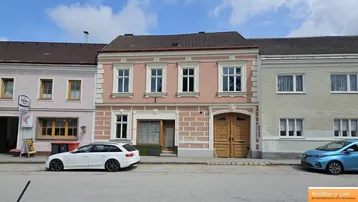 Rosa gestrichenes historisches Gebäude mit weißen Fensterrahmen und Holztüren an einer Straße.