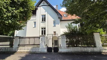 Historisches Gebäude mit weißer Fassade, rotem Dach und einem schmiedeeisernen Zaun.
