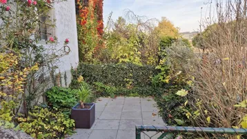 Kleiner, gepflasterter Gartenbereich mit üppiger Bepflanzung und Blick ins Grüne.