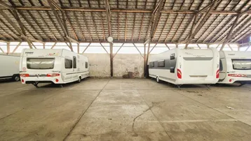Geräumige Lagerhalle mit Holzbalkenkonstruktion und mehreren geparkten Wohnwagen auf Betonboden.