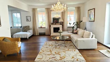 Elegantes Wohnzimmer mit Kronleuchter, Kamin, Parkettboden und großen Fenstern.
