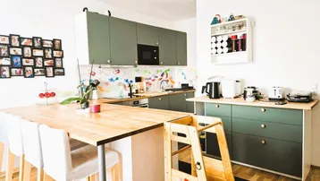 Moderne Küche mit grünen Schränken, Holzarbeitsplatte und Kücheninsel mit Barhockern, ideal für Familien.