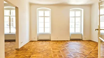 Helles Zimmer mit kunstvollem Parkettboden, hohen Fenstern und weiß gestrichenen Wänden.
