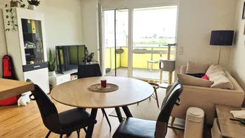 Heller Wohn- und Essbereich mit Holzboden, modernem Esstisch und Zugang zu einem Balkon.