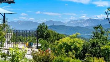 Terrasse mit atemberaubendem Bergblick und üppiger grüner Landschaft unter blauem Himmel.