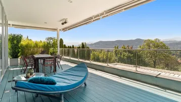 Geräumige überdachte Terrasse mit blauer Holzterrasse, Essbereich und atemberaubendem Bergblick.