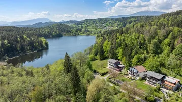 Malerische Luftaufnahme eines Sees, umgeben von Wäldern und Bergen, mit Häusern am Ufer.