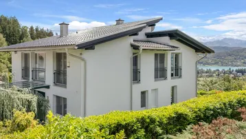 Modernes Haus mit weißer Fassade, dunklem Dach und weitem Blick auf den See und die Berge.