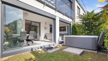 Außenansicht des Hauses mit Garten, Whirlpool und großen Glasfronten zum Innenbereich.