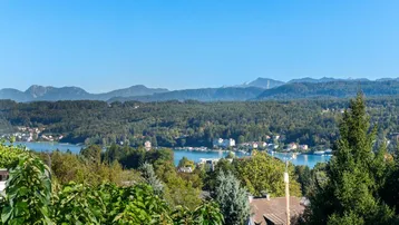 Panoramablick auf den See und die umliegende Berglandschaft unter klarem blauem Himmel.