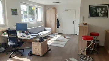 Heller Wohnbereich mit Arbeitsplatz, Sofa und kleiner Bar, ausgestattet mit Laminatboden und großen Fenstern.