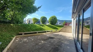 Große gepflasterte Terrasse mit Zugang zum Garten, umgeben von Grünflächen und mit Blick auf die Berge.