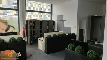 Helles Büro mit großen Fenstern, modernen Arbeitsplätzen und Blick auf umliegende Gebäude.