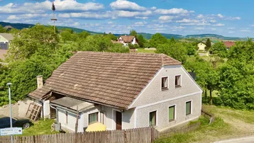 Luftaufnahme eines traditionellen Hauses mit Ziegeldach und heller Fassade, umgeben von viel Grün in ländlicher Umgebung.