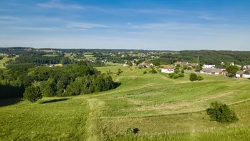 Weitläufige Luftaufnahme der grünen, hügeligen Landschaft mit verstreuten Häusern unter blauem Himmel.