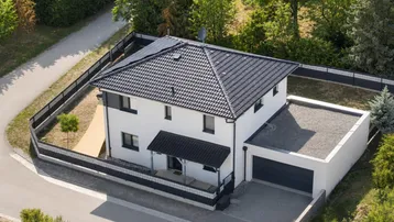 Luftaufnahme eines modernen Einfamilienhauses mit dunklem Dach, Solaranlage und Garage.