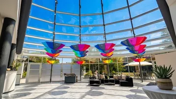 Heller, lichtdurchfluteter Lounge-Bereich mit Glasdach und farbenfrohen Regenschirm-Dekorationen.