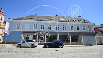Blaues Gebäude mit Geschäften im Erdgeschoss und gepflasterter Straße davor.