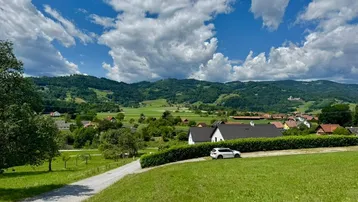 Idyllische Landschaft mit grünen Hügeln, Häusern und einer Straße unter blauem Himmel.