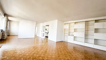 Helles, geräumiges Wohnzimmer mit Fischgrätparkettboden und integrierten weißen Einbauregalen.