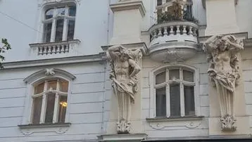 Klassisches Altbaugebäude mit reich verzierten Fassaden, Säulen und einem kleinen Balkon an einer belebten Straße.