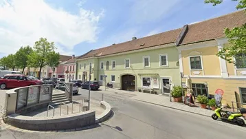 Blick auf eine belebte Straße mit traditionellen Gebäuden und geparkten Autos unter blauem Himmel.