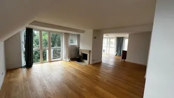 Geräumiges Wohnzimmer mit Holzboden, Kamin und Zugang zu einem französischen Balkon.