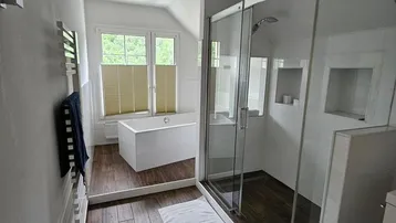 Modernes Badezimmer mit begehbarer Dusche, Badewanne und Fenster unter Dachschräge.