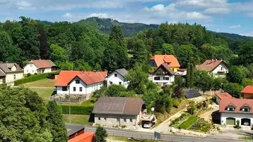 Malerische Landschaft mit mehreren Häusern und grünen Hügeln unter blauem Himmel.