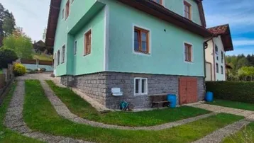Freistehendes Haus mit grüner Fassade, rotem Mansarddach und gepflasterter Auffahrt.