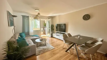 Helles Wohn- und Esszimmer mit Holzboden, bequemer Couch und Zugang zum Balkon.