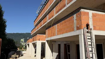 Neubau im Rohbauzustand mit sichtbaren Ziegelwänden und Betonelementen unter blauem Himmel.