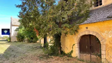 Altes Gebäude mit verwitterter Fassade, Holztür und üppiger Vegetation im Außenbereich.