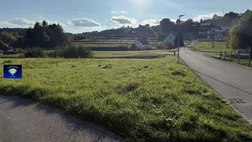 Sonniges Grundstück an einer Kreuzung mit Blick auf die umliegende Landschaft und Häuser am Hang.